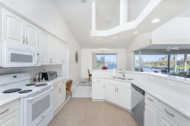 kitchen with white appliances, ceiling fan with notable chandelier, sink, vaulted ceiling, and white cabinetry