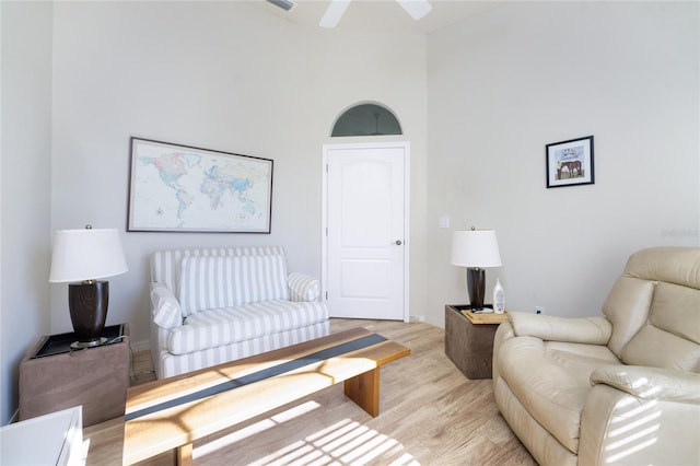 living room featuring a towering ceiling, light wood-type flooring, and ceiling fan