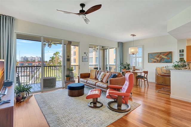 living room featuring ceiling fan with notable chandelier, light wood-type flooring, and a healthy amount of sunlight