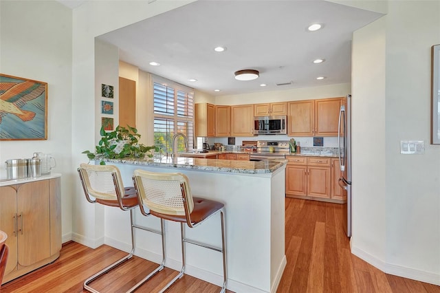 kitchen featuring light stone countertops, appliances with stainless steel finishes, light wood-type flooring, kitchen peninsula, and light brown cabinets