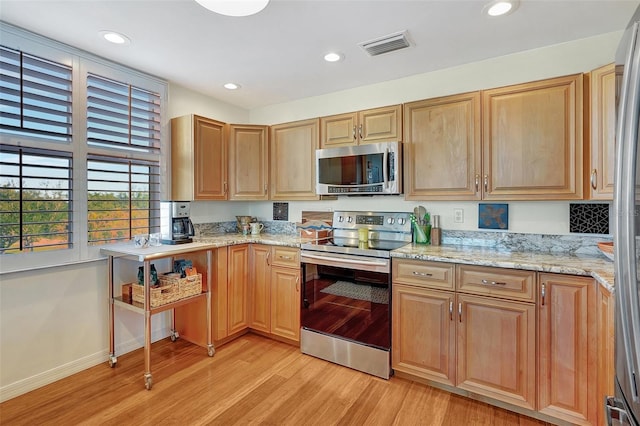 kitchen with appliances with stainless steel finishes, light hardwood / wood-style floors, and light stone counters