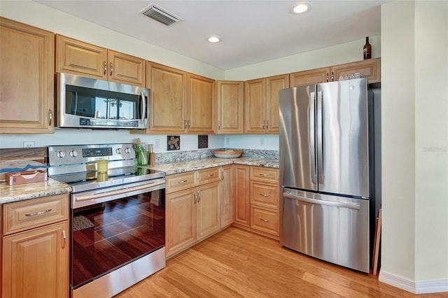 kitchen with light stone countertops, appliances with stainless steel finishes, and light hardwood / wood-style flooring