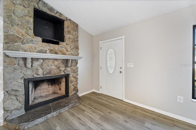 foyer entrance with hardwood / wood-style floors, plenty of natural light, a stone fireplace, and vaulted ceiling