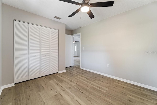 unfurnished bedroom featuring a textured ceiling, a closet, light hardwood / wood-style floors, and ceiling fan