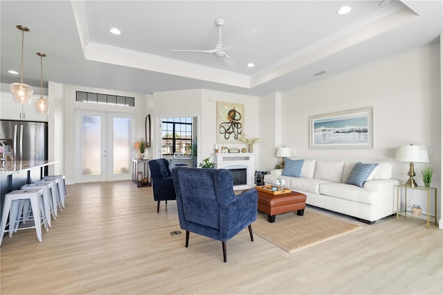 living room featuring a raised ceiling, light wood-type flooring, and french doors