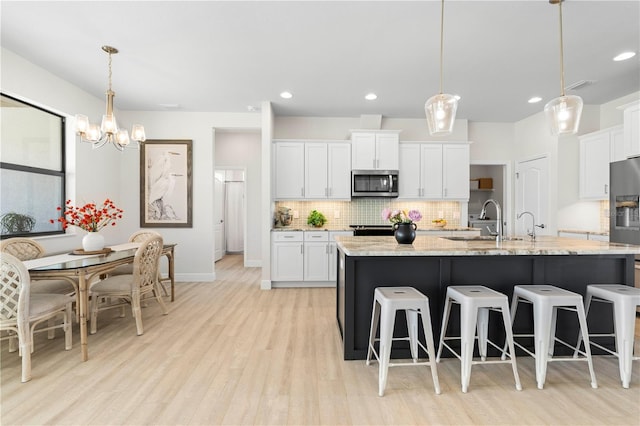 kitchen with white cabinets, light wood-type flooring, decorative light fixtures, and an island with sink