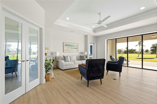 living room with french doors, light wood-type flooring, ornamental molding, a tray ceiling, and ceiling fan