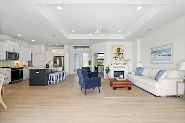 living room with light wood-type flooring, a raised ceiling, ceiling fan, and sink