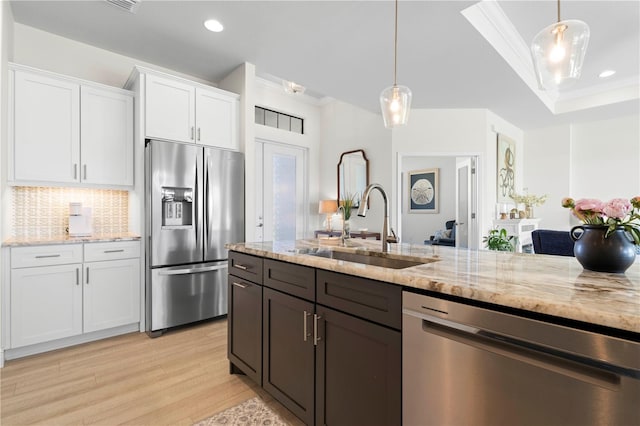 kitchen with pendant lighting, white cabinets, sink, ornamental molding, and appliances with stainless steel finishes