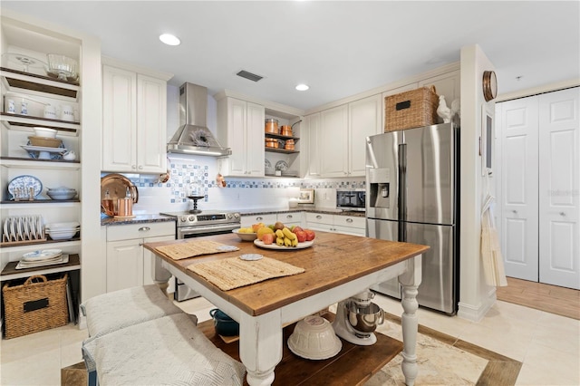 kitchen featuring white cabinets, wall chimney range hood, light tile patterned floors, tasteful backsplash, and stainless steel appliances