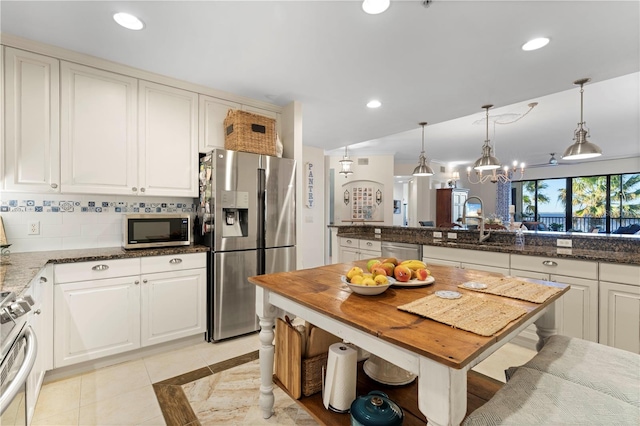 kitchen with white cabinetry, dark stone counters, pendant lighting, light tile patterned floors, and appliances with stainless steel finishes