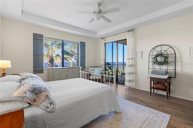 bedroom featuring multiple windows, hardwood / wood-style floors, a tray ceiling, and ceiling fan