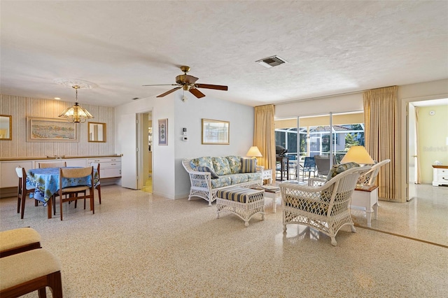 living room featuring ceiling fan with notable chandelier and a textured ceiling