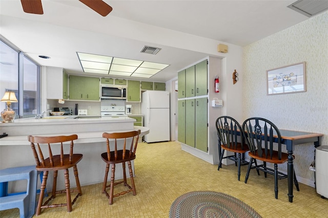 kitchen featuring a kitchen bar, kitchen peninsula, white appliances, ceiling fan, and green cabinets