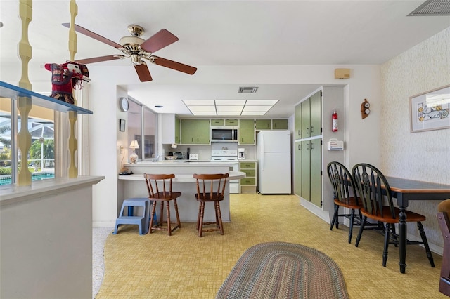 kitchen featuring ceiling fan, green cabinets, kitchen peninsula, white appliances, and a breakfast bar