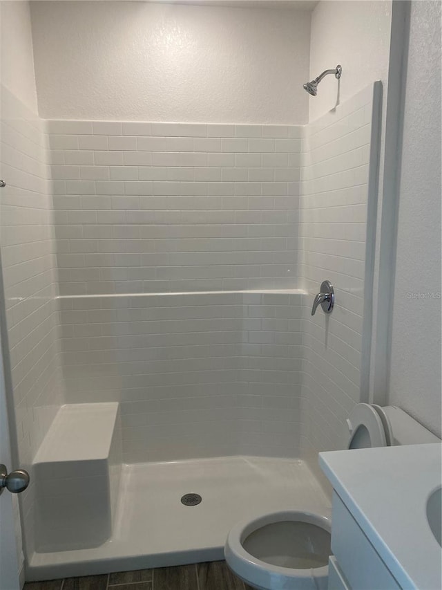 bathroom with toilet, a tile shower, and vanity