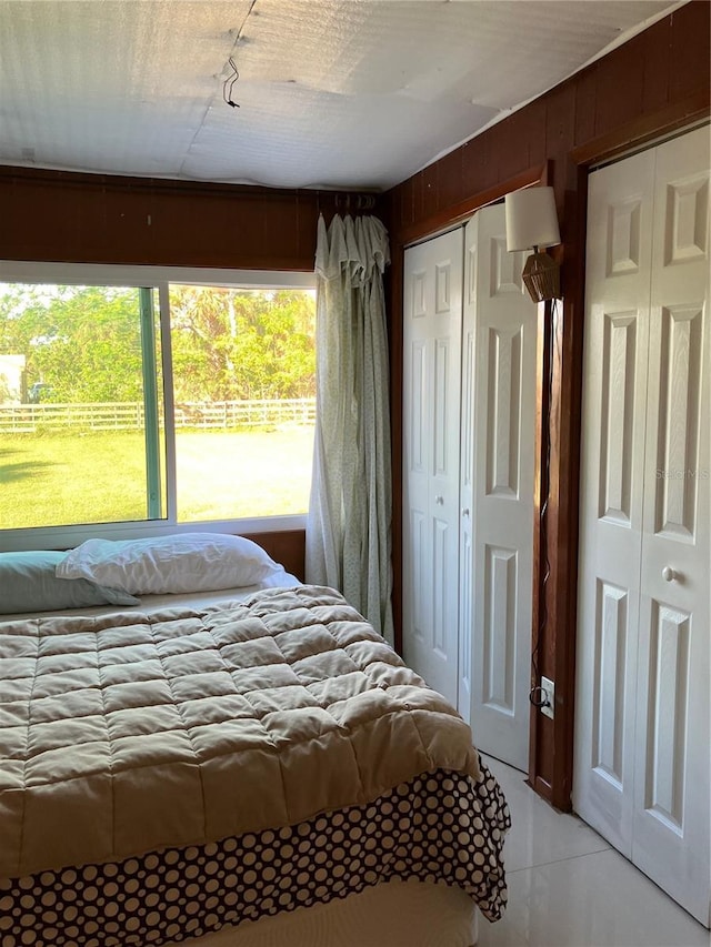 bedroom with light tile patterned flooring, wooden walls, and two closets