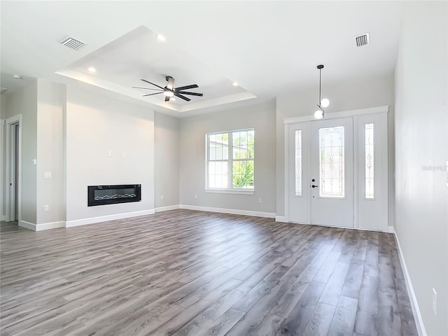 unfurnished living room with a raised ceiling, ceiling fan, and hardwood / wood-style floors