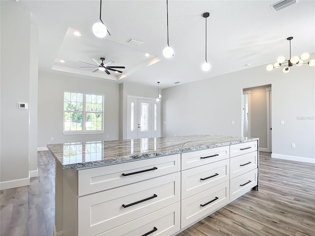 kitchen featuring white cabinets, light stone counters, light wood-type flooring, and hanging light fixtures