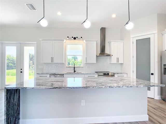 kitchen featuring white cabinets, decorative light fixtures, wall chimney range hood, and a large island