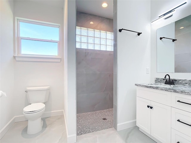 bathroom with tiled shower, a wealth of natural light, vanity, and toilet