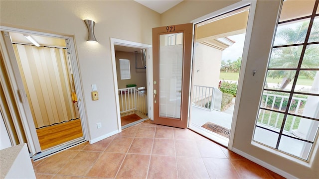 doorway to outside with a wealth of natural light, light tile patterned flooring, and lofted ceiling