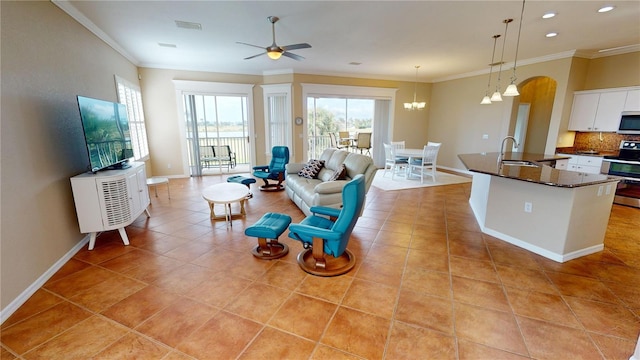 living room with ceiling fan with notable chandelier, sink, light tile patterned floors, and crown molding