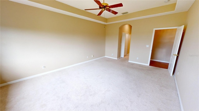 unfurnished room with a tray ceiling, light carpet, and ceiling fan