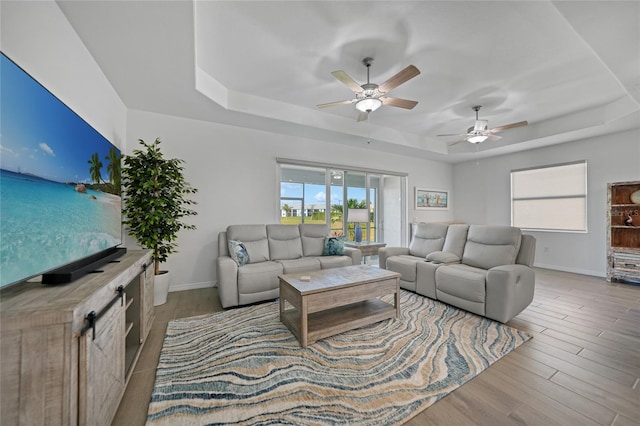 living room featuring ceiling fan, light hardwood / wood-style floors, and a tray ceiling