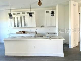 kitchen featuring dark hardwood / wood-style flooring, sink, pendant lighting, a center island with sink, and white cabinets