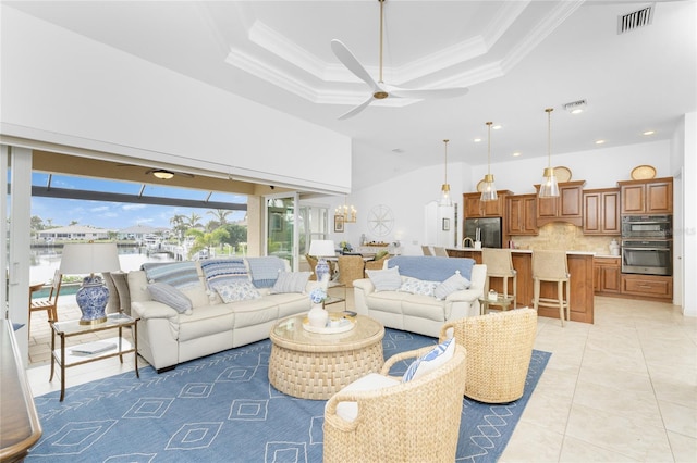 living room featuring light tile patterned floors, ceiling fan, a tray ceiling, and crown molding