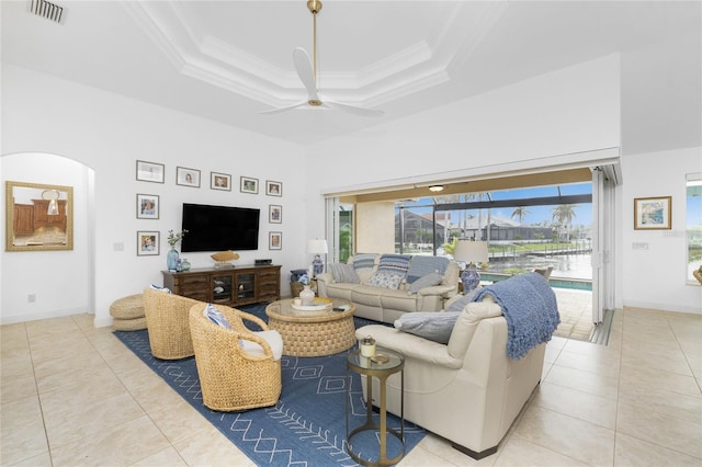 living room with a raised ceiling, a towering ceiling, ceiling fan, light tile patterned flooring, and ornamental molding