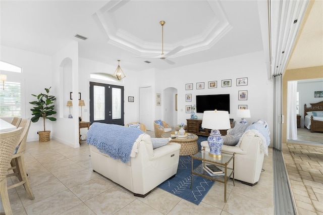 tiled living room with a raised ceiling, ceiling fan, ornamental molding, and french doors