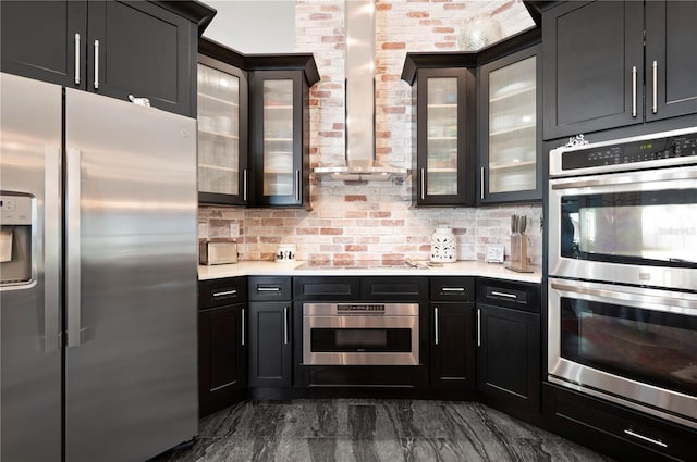 kitchen with brick wall, appliances with stainless steel finishes, tasteful backsplash, and wall chimney range hood