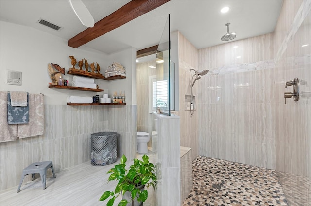 bathroom featuring toilet, a tile shower, tile walls, and beamed ceiling