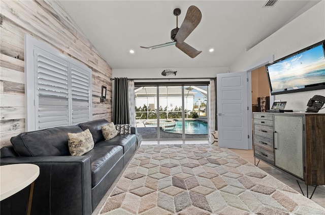 living room with ceiling fan, lofted ceiling, wood walls, and light wood-type flooring