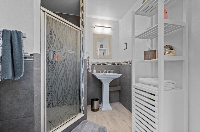 bathroom with hardwood / wood-style flooring, tile walls, an enclosed shower, a textured ceiling, and sink