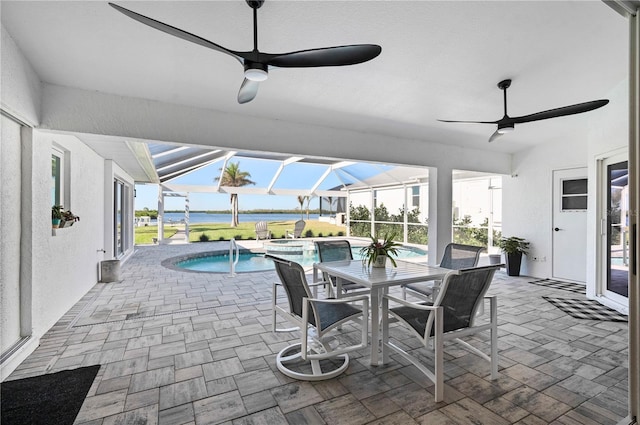 view of patio featuring ceiling fan, glass enclosure, a swimming pool with hot tub, and a water view