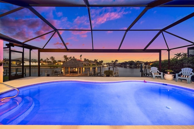 pool at dusk featuring glass enclosure, a patio, a water view, and a gazebo