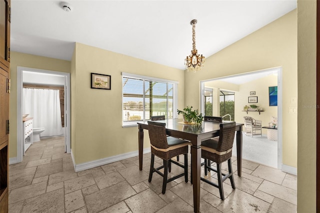 dining space featuring lofted ceiling, stone tile flooring, a notable chandelier, and baseboards