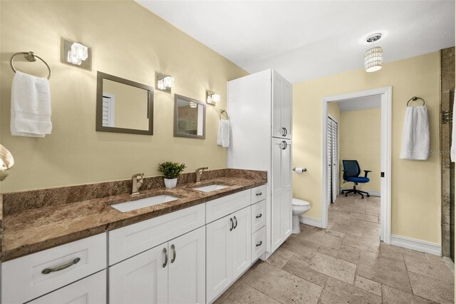 bathroom featuring a closet, stone tile flooring, a sink, and toilet