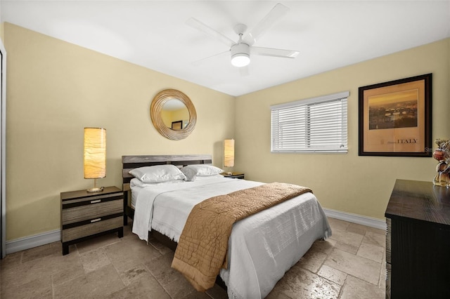 bedroom with ceiling fan, stone tile flooring, and baseboards