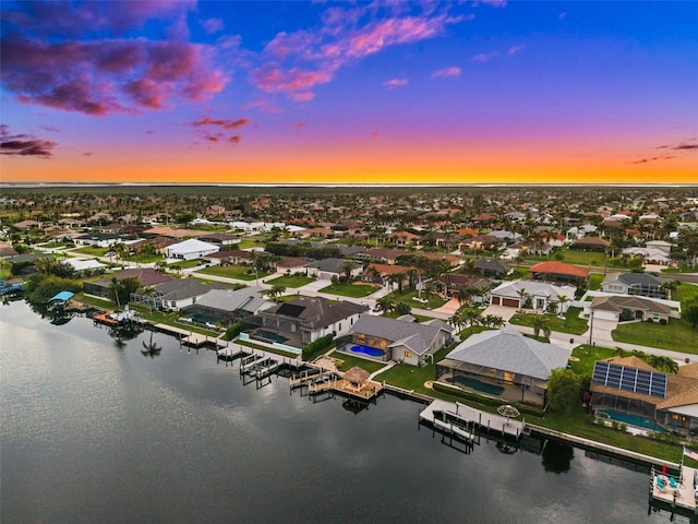 aerial view at dusk with a water view and a residential view