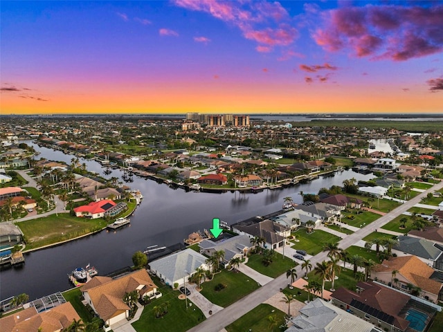 aerial view at dusk featuring a water view and a residential view