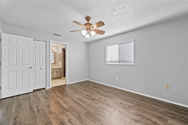 unfurnished bedroom featuring hardwood / wood-style floors, a textured ceiling, a closet, ceiling fan, and ensuite bathroom