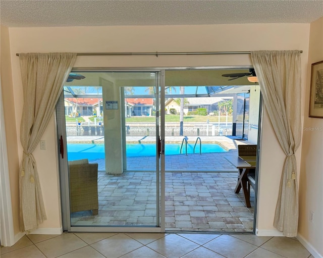 doorway to outside with a textured ceiling, tile patterned floors, and ceiling fan