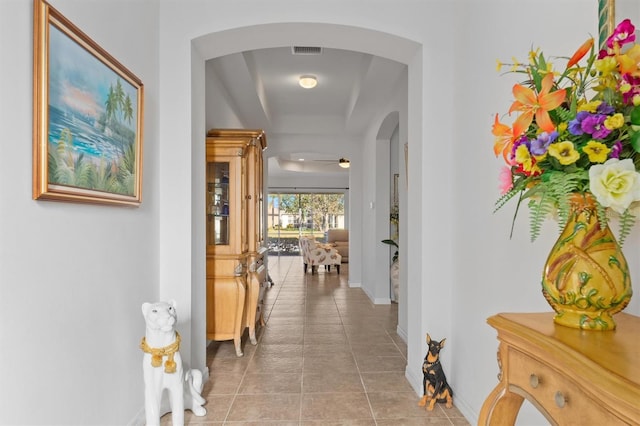 hall featuring arched walkways, visible vents, baseboards, and light tile patterned flooring