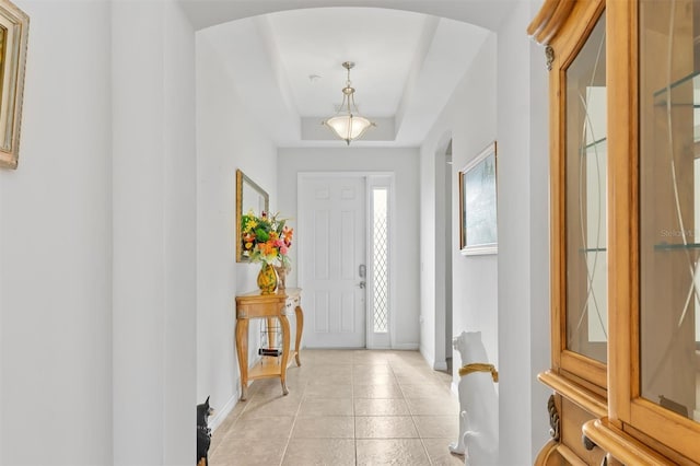 entryway with a tray ceiling, light tile patterned floors, baseboards, and arched walkways