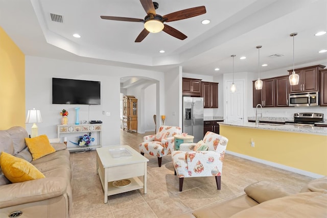 tiled living room featuring a raised ceiling, ceiling fan, and sink