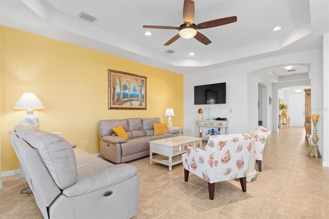 living room featuring ceiling fan, a raised ceiling, and light tile patterned floors